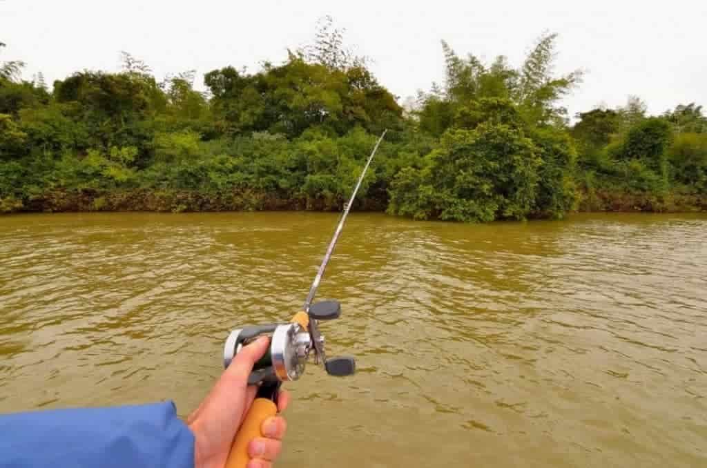 man fishing in muddy water river with casting rig from a boat