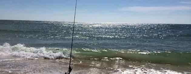small waves while surf fishing on a beautiful blue sky day pole in water waiting on fish to bite