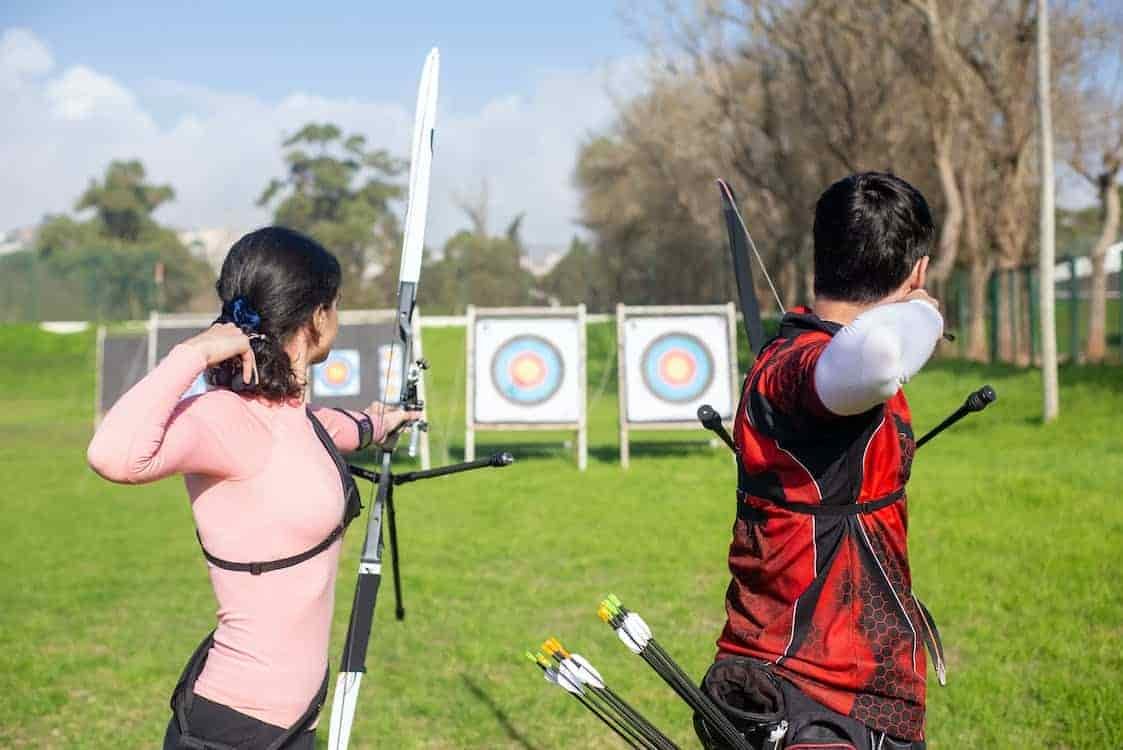 man and woman practicing archery using targets in open field