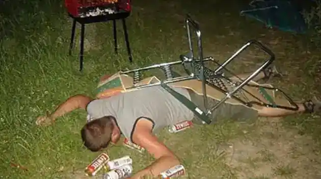 intoxicated man laying face down with beer cans all around him chair still on him