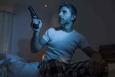 man holding gun in bed just woke up defending himself