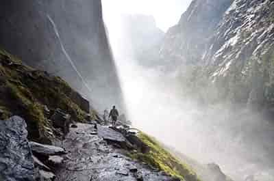 heavy mist mountain morning 2 hikers walking through mountain passage along waters edge